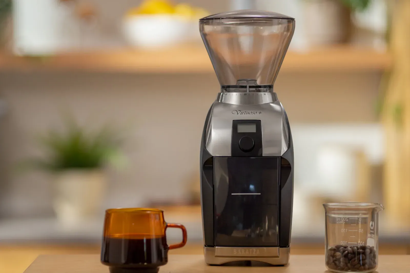 Un moulin Baratza Virtuoso+ sur un plan de travail en bois, entre un verre de café et un bocal de grains