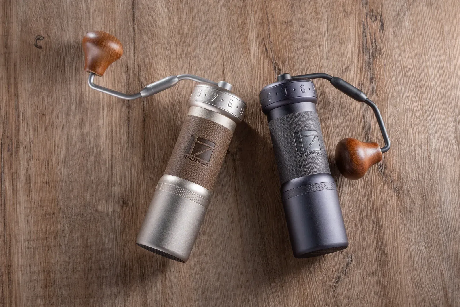 Deux moulins manuels 1Zpresso, l'un argenté et l'autre gris foncé, posés sur une table en bois