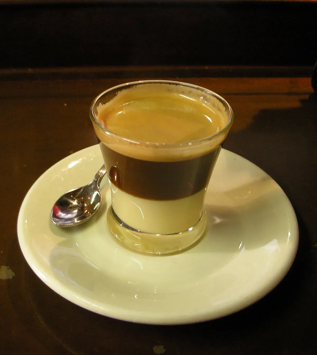 Un café bombón dans un petit verre évasé sur une soucoupe avec une cuillère, l'espresso posé sur le lait concentré