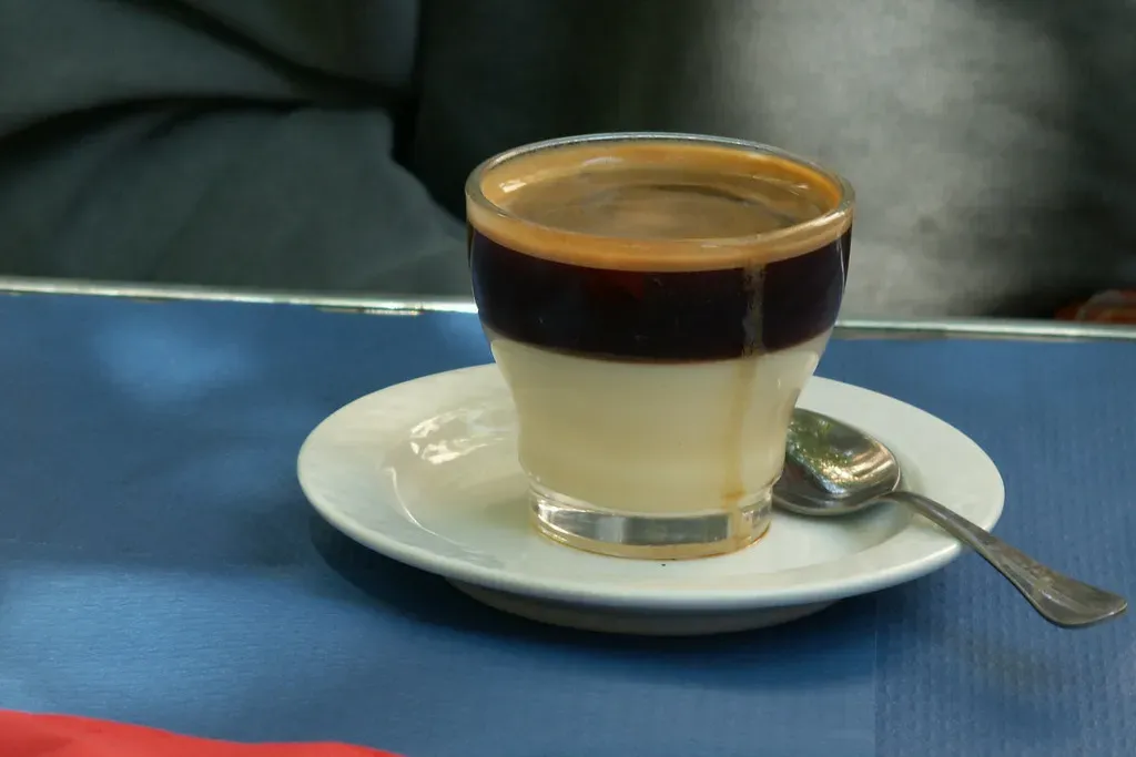 Un café bombón dans un petit verre sur une soucoupe, une bande d'espresso sombre au-dessus du lait concentré blanc