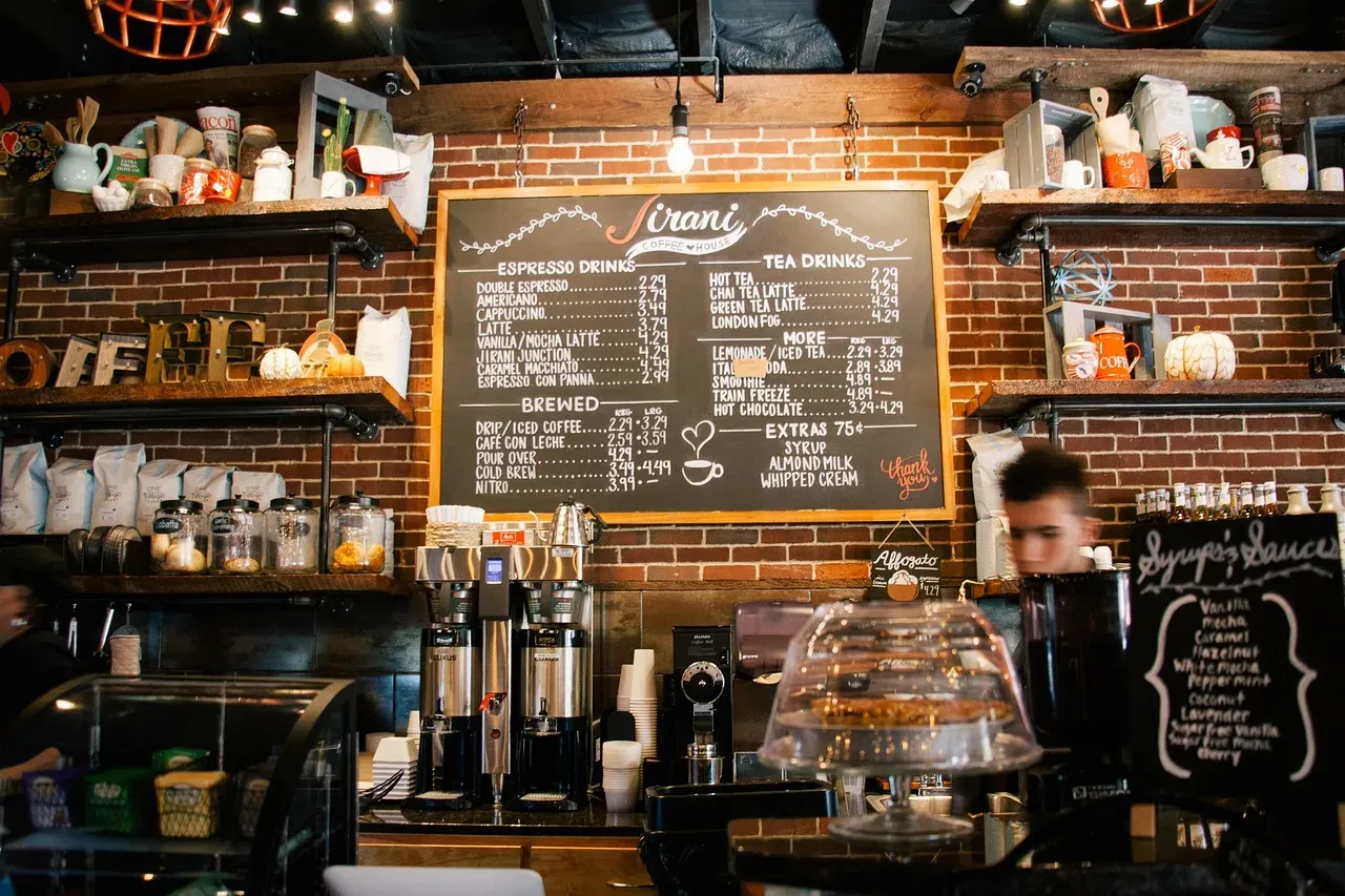 Un menu de café sur tableau noir, séparé en une colonne espresso et une colonne filtre, au-dessus de deux percolateurs posés sur le comptoir