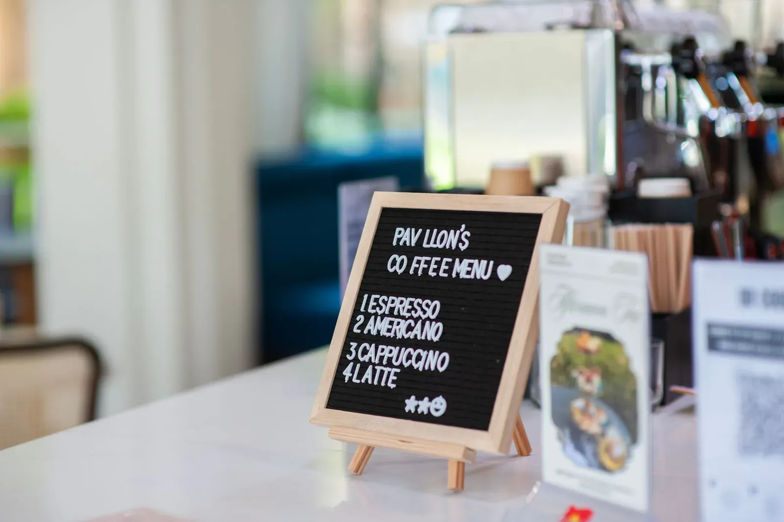 Un petit menu à lettres posé sur le comptoir d'un café, listant espresso, americano, cappuccino et latte