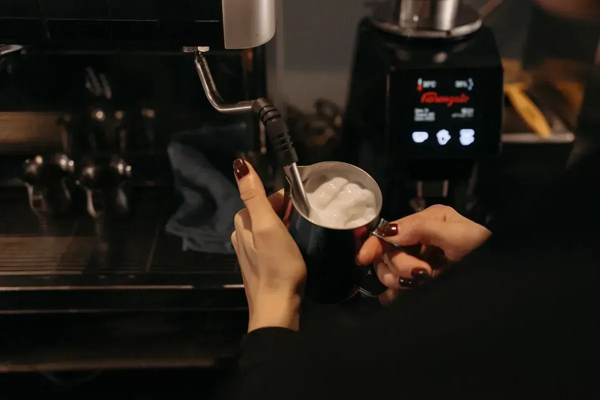 Une buse vapeur maintenue juste sous la surface du lait dans un pichet en inox