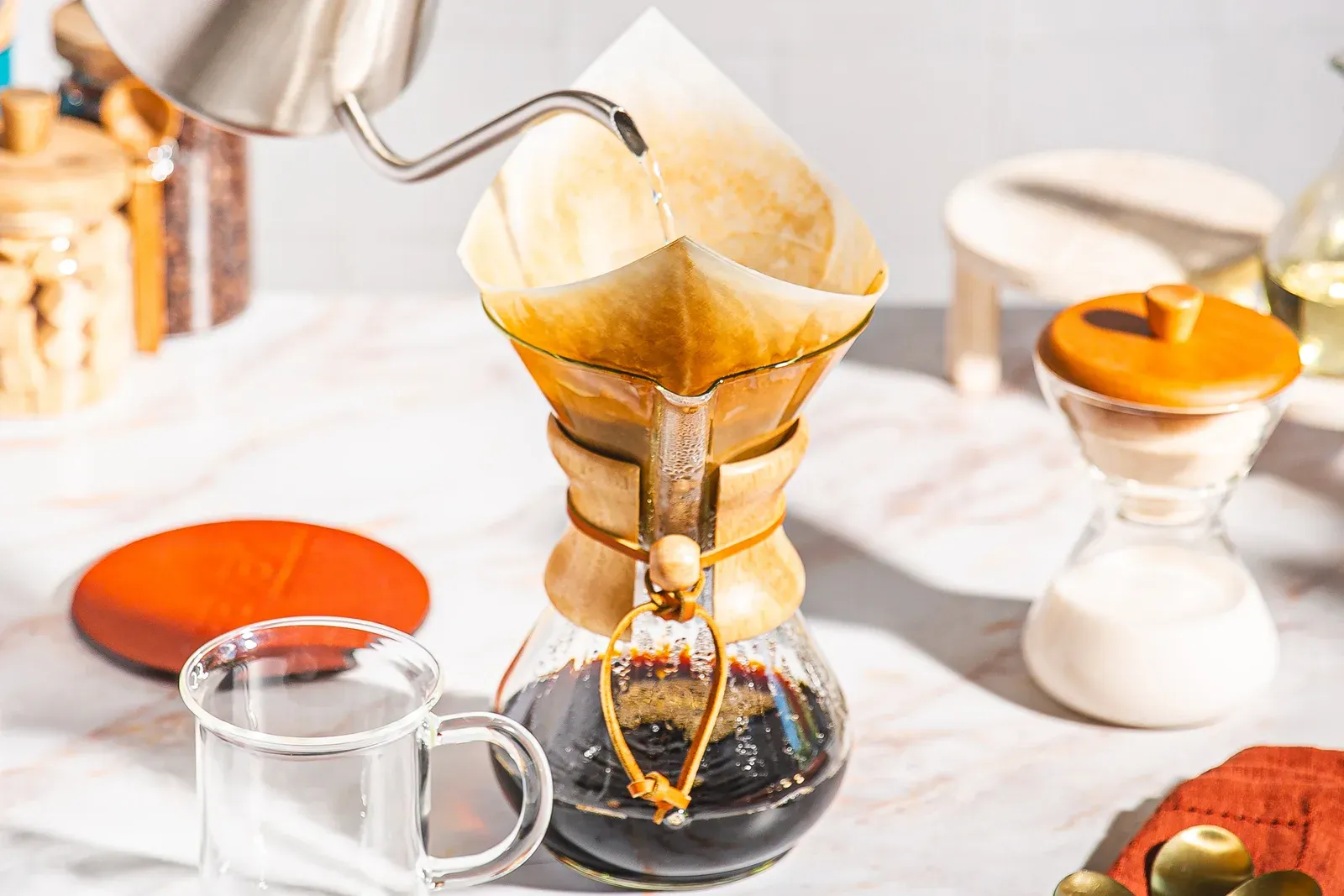 Une bouilloire à col de cygne verse de l'eau dans un filtre en papier naturel posé sur une Chemex Classic, le café déjà dans le ballon du bas