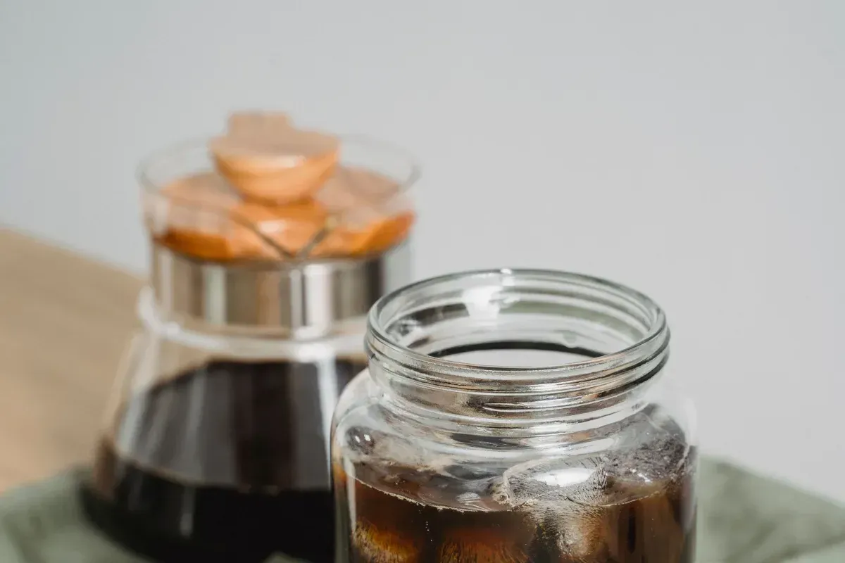 Un bocal de cold brew noir sur glace, à côté de la cafetière