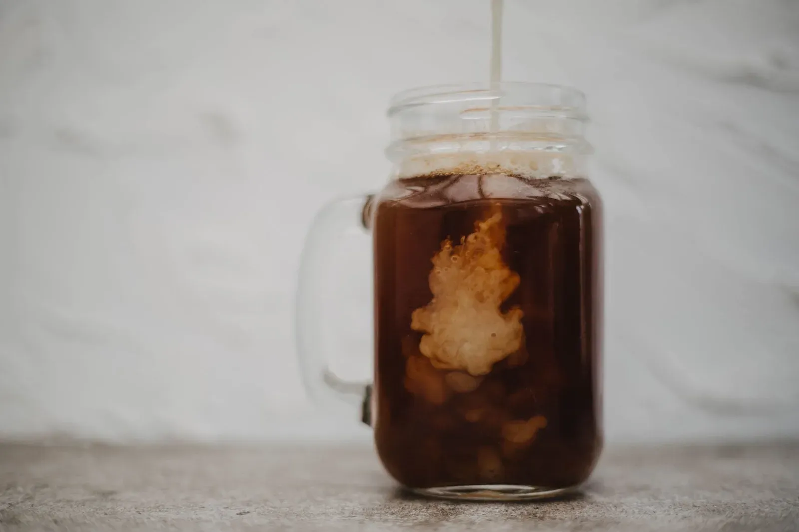 Un cold brew en bocal de verre, la crème qui descend dedans