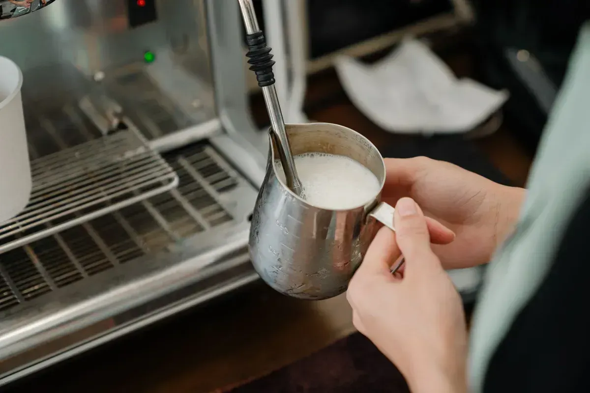Un barista fait rouler le lait dans un pichet en inox sous la buse vapeur