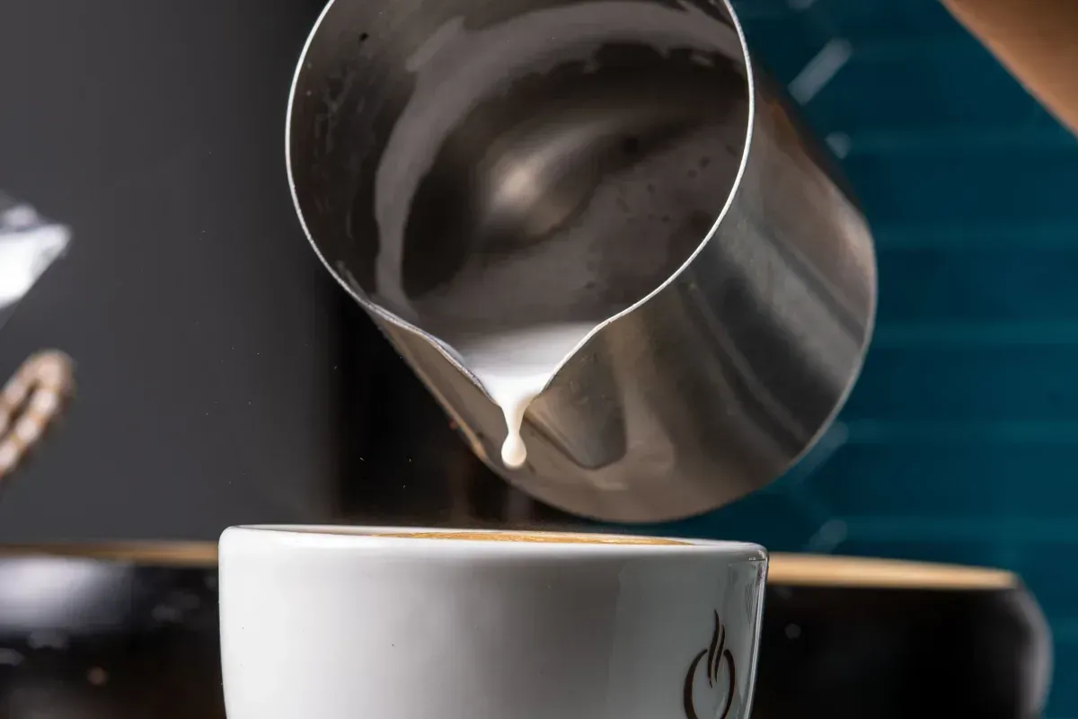 Un barista verse du lait texturé dans une tasse blanche inclinée