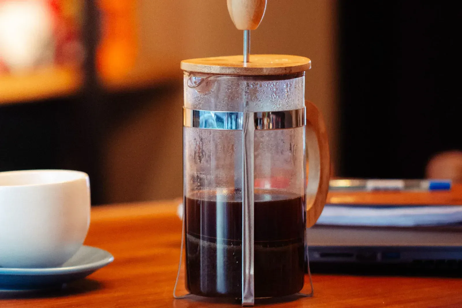Une cafetière à piston pleine de café sur une table en bois, le piston encore relevé