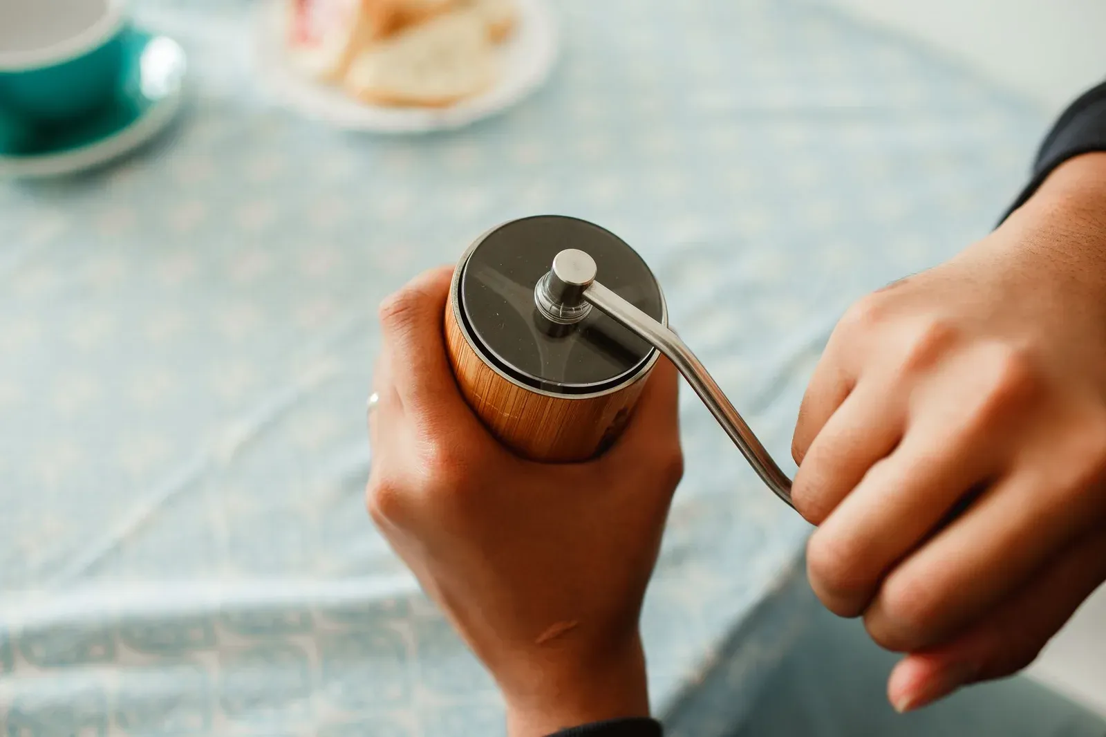 A person turning the crank of a hand grinder at a table
