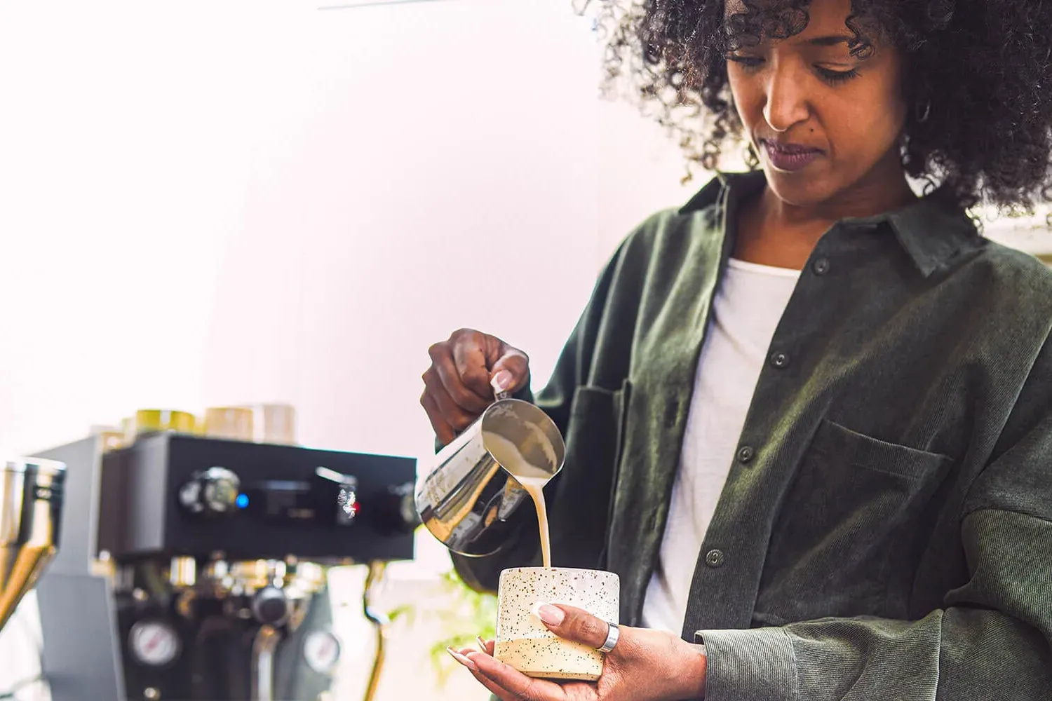 Une barista verse du lait moussé dans une tasse, à côté d'une Linea Micra noire