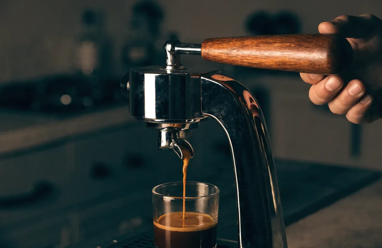 Une machine espresso à levier à ressort chromée, levier relevé, une tasse en attente sous le groupe