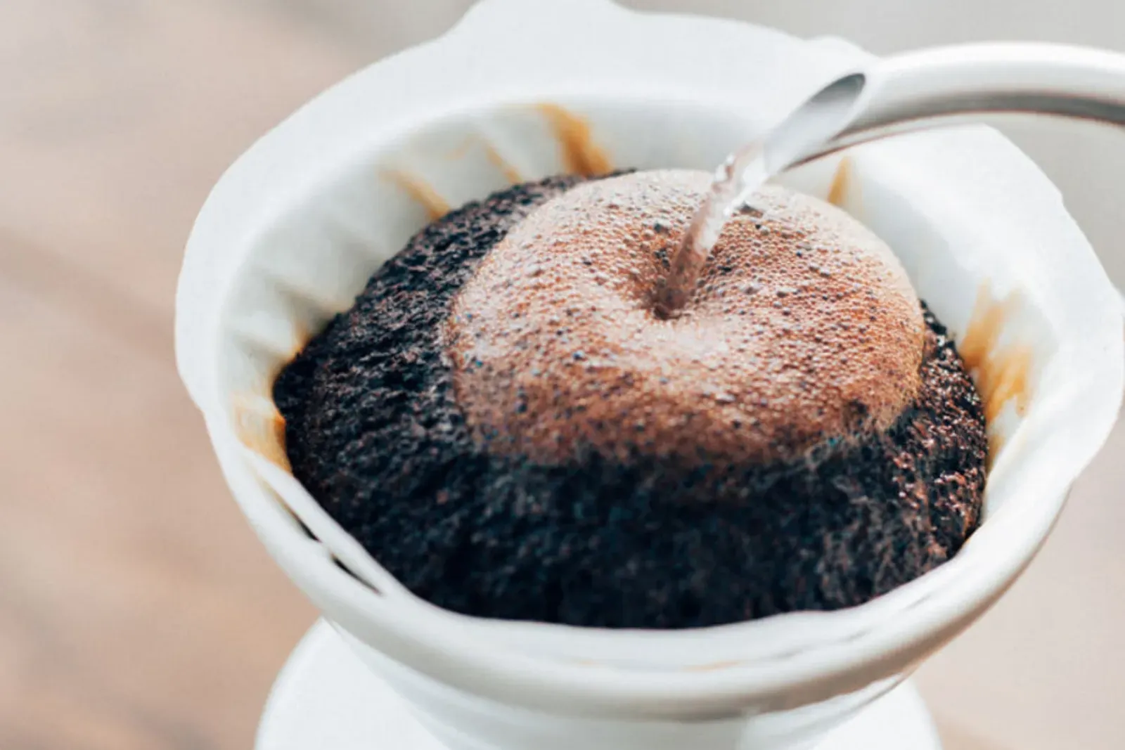 De l'eau chaude versée sur le café qui gonfle dans un dripper Hario V60 en céramique blanche