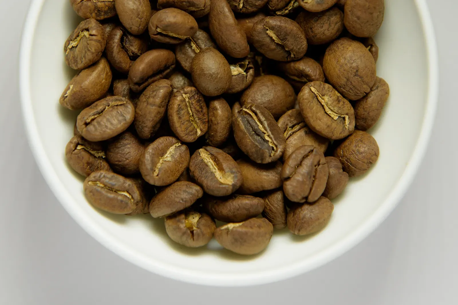 Des grains de café fraîchement torréfiés dans un bol blanc, vus de dessus