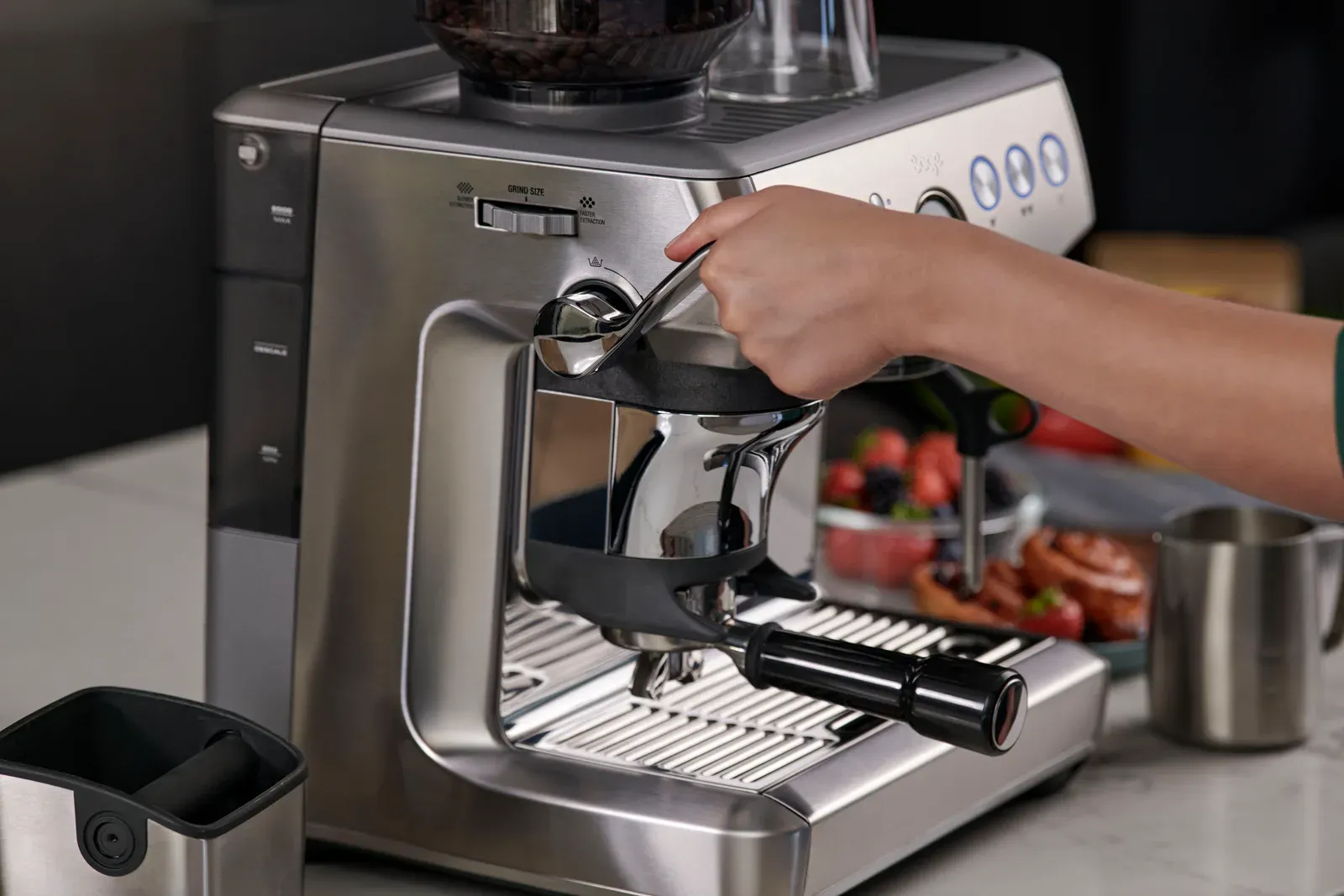 Une main abaisse le levier de tassage assisté d'une machine espresso inox à moulin intégré