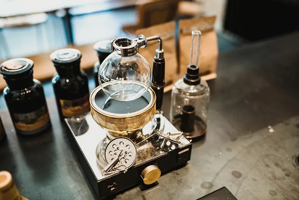 Un siphon en verre sur un petit brûleur, au comptoir d'un café, à côté de bocaux de café