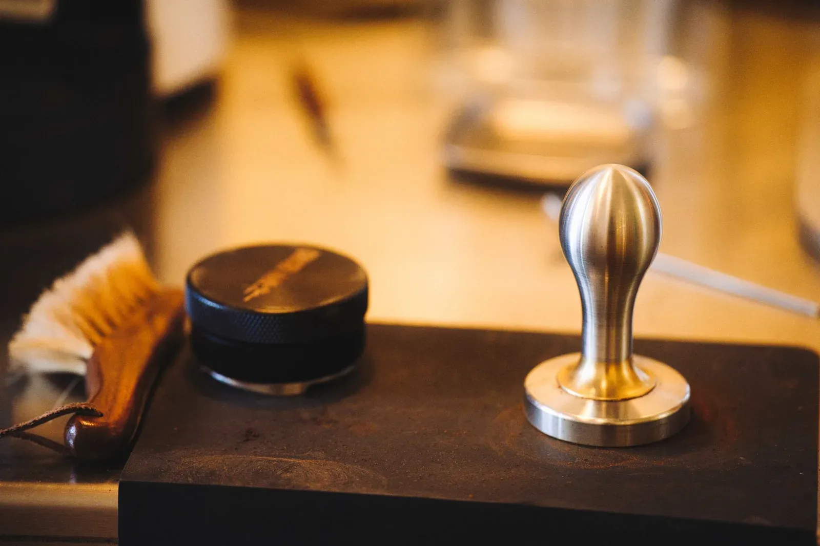 A tamper, a brush and tools laid out on a barista counter