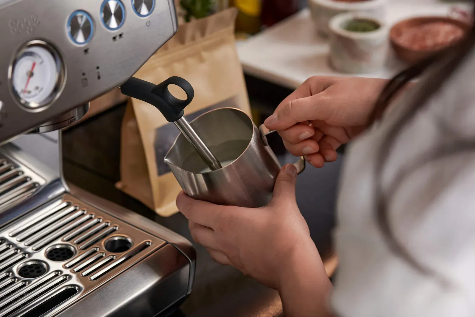 Du lait chauffé dans un pichet en inox sous la buse vapeur d'une machine espresso Sage