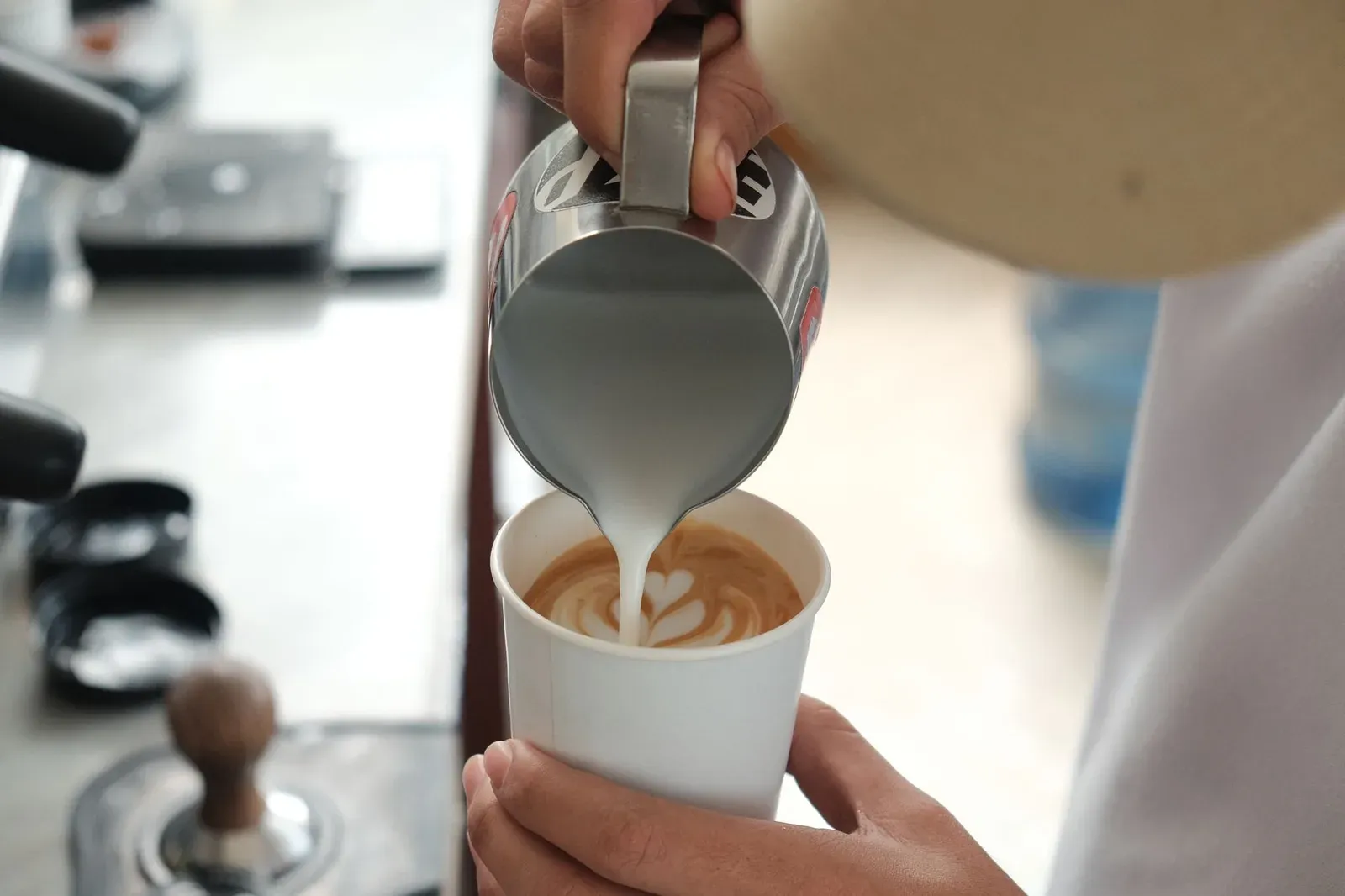 Un barista versant du lait dans une tasse pour faire un latte art