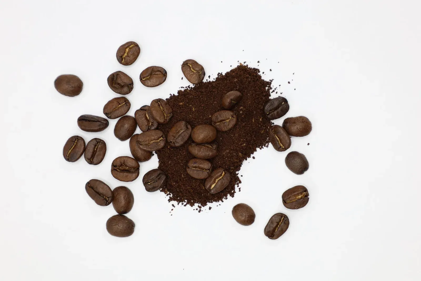 Des grains entiers à côté d'un tas de café moulu sur fond blanc